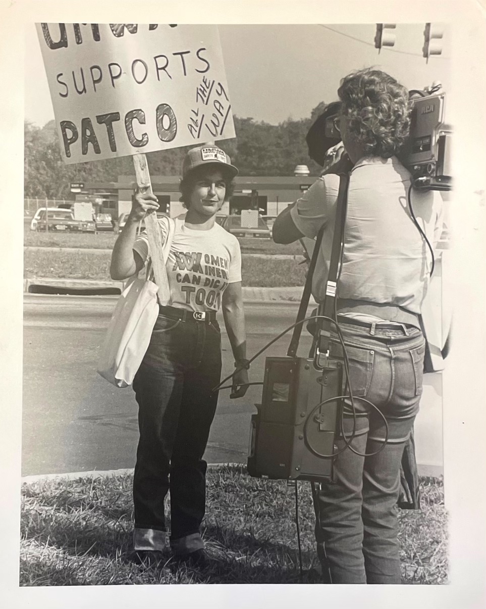 black and white photo of a woman holding a sign in front of a camera operator
